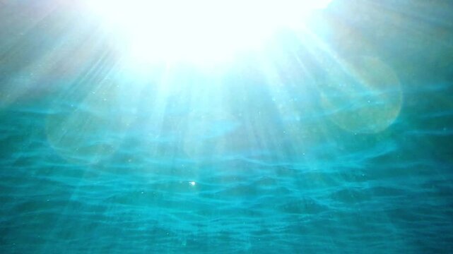 A slow-motion shot of an underwater sea background, sunlight penetrating and reflecting of sea surface. deep undersea. light rays shining through. Dark blue ocean surface seen from under water.