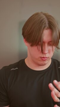 Young man featuring pale chestnut locks and dark attire. Around four and half seconds initial segment shows. Young man winds fabric over both appendages to protect wrists