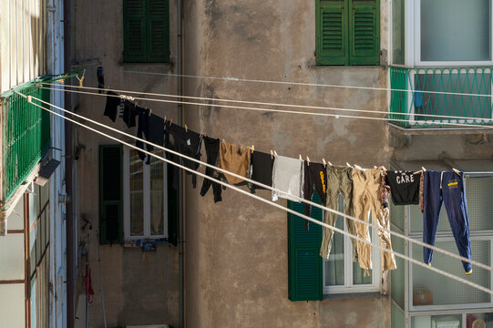 Facciate storiche con persiane verdi e panni stesi al sole tra i palazzi. Scena urbana autentica ideale per temi vita quotidiana, Mediterraneo, architettura e atmosfera residenziale.