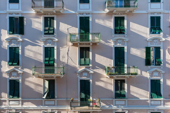 Facciata residenziale con persiane verdi, balconi in ferro battuto e giochi di luce e ombre. Scena urbana elegante ideale per temi architettura, Mediterraneo, citt&agrave; e atmosfera residenziale.