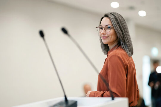 Confident businesswoman wearing eyeglasses speaking into microphone at conference