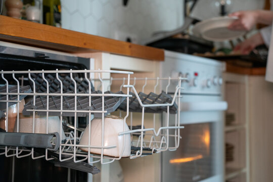 Open dishwasher rack with clean cups while boy puts dishes away in home kitchen. Household chores, responsibility, independence, domestic skills, family routine, organization, everyday life
