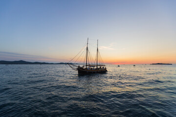 Fototapeta premium Tall ship two mast sailing vessel at sunset on calm sea golden hour water.