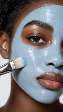 Beautiful young woman applying blue clay facial mask on her face