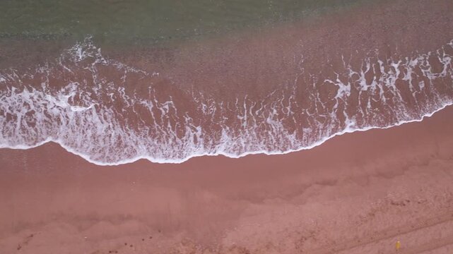 Aerial top-down video of waves breaking on Black Sea shore in ambient early morning light.