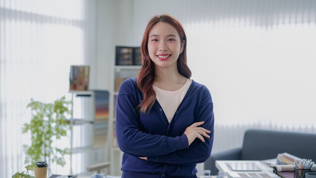 Young Asian woman furniture designer standing confidently with arms crossed in bright modern studio office with copy space