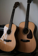 Fototapeta premium Two acoustic guitars with light wood bodies and dark fretboards leaning against a wall, musical instruments, the musical instruments are positioned side by side, their strings, bridges