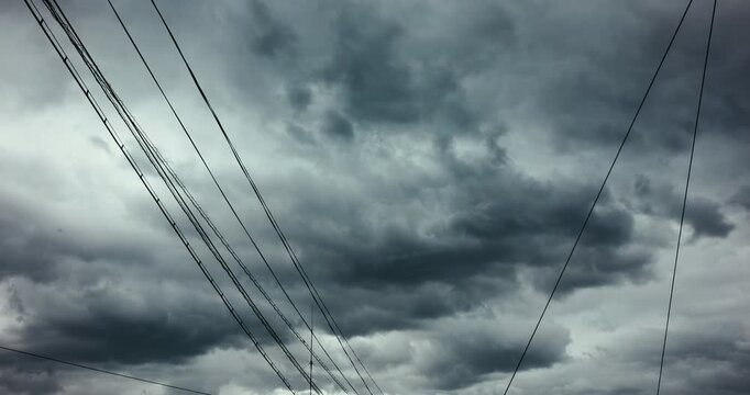 Cinematic time lapse of dramatic storm clouds moving rapidly across a wide urban sky, framed by a network of overhead utility and communication wires. 