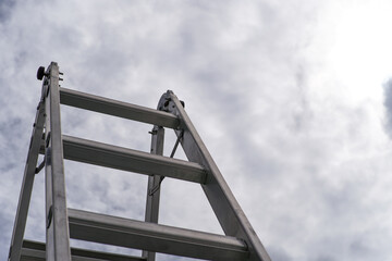 Naklejka premium Sturdy Aluminum Folding Ladder Viewed from Below Against Cloudy Sky