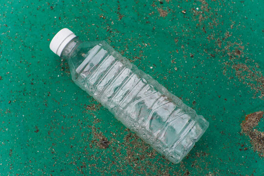 Empty Plastic Water Bottle with White Cap on a Sandy Green Surface