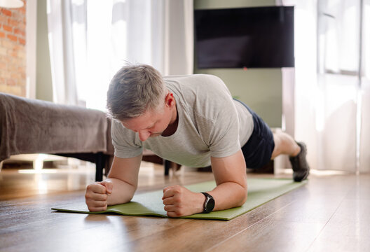 Man holds plank position on exercise mat during morning fitness routine in living room