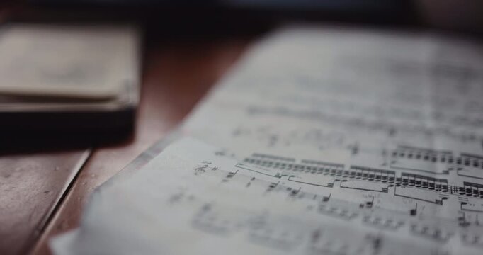 Cinematic close-up of printed sheet music resting on a  wooden desk in a professional workspace.  large open musical score with clearly visible staff lines. music notes Moscow Russia 07.06.2026