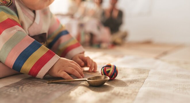 Baby in hanbok reaching for spoon and yarn ball during doljabi ceremony