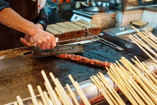 Chef grilling meat skewer with mala on hot flat top griddle in commercial kitchen night market
