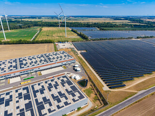 Fototapeta premium Solar panels and wind turbines are present in a large energy facility in an open area during daytime under clear skies