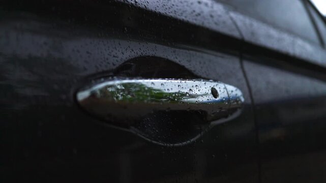 Close-up of chrome car door handle with water drops on dark vehicle in rain. Vehicle paint protection, ceramic hydrophobic coating, auto detailing, and rainy season concept.