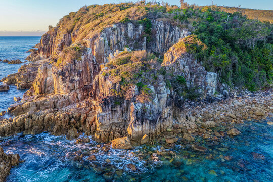 Aerial view of the rugged rocky headland at Diamond Head surrounded by clear turquoise ocean water, showcasing the natural coastal landscape and pristine marine environment on the Mid North Coast
