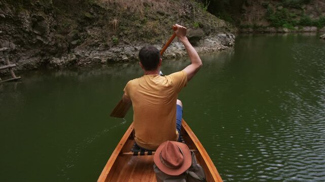 Slow motion of man paddling a wooden canoe across a calm lake