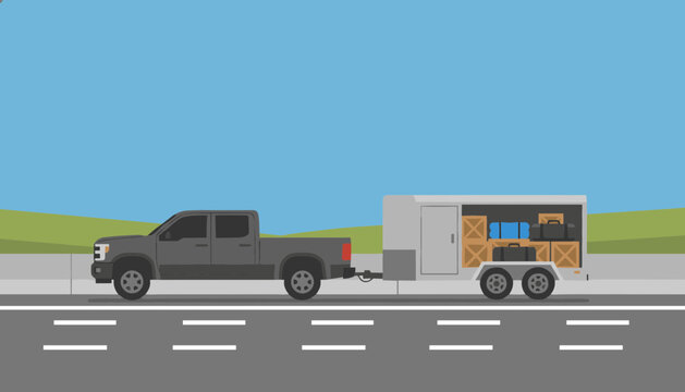 Dark pickup truck towing a utility trailer filled with packed wooden cargo boxes along a highway road.
