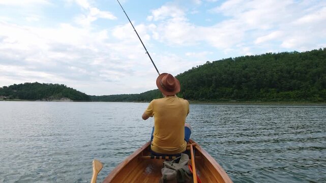 Rear view of a man fishing from a wooden canoe 