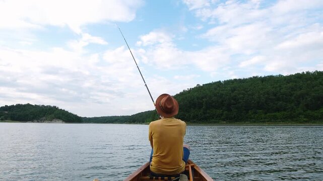 Rear view of a man fishing from a wooden canoe on a forest lake