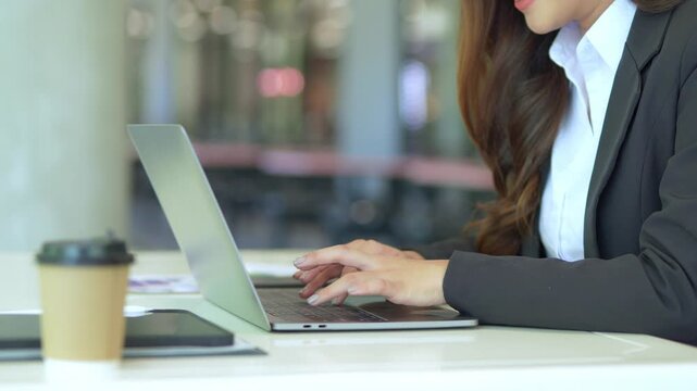 Asian businesswoman working at desk using laptop and notebook talking to client or office building, slow motion footage