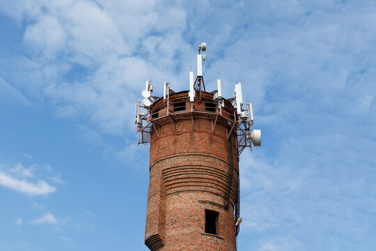 Old brick water tower repurposed with modern cellular network antennas against blue sky with clouds