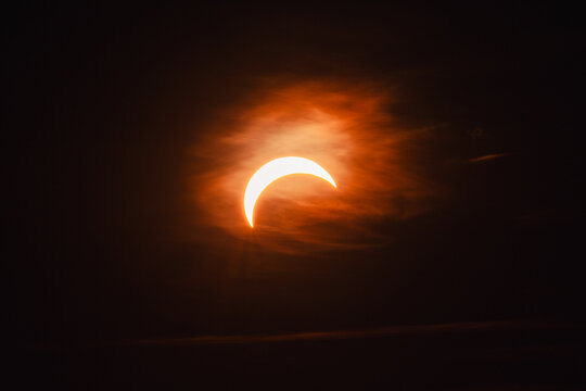 View of a partial solar eclipse with the sun appearing as a bright crescent behind thin, wispy clouds in the dark sky, Merikula, Harju maakond, Estonia.
