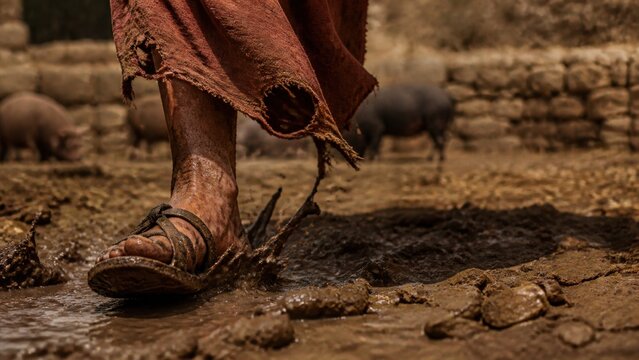 Barefoot man in worn clothing walking through muddy ground among pigs, portraying the prodigal son&rsquo;s hardship, repentance, and return in a biblical parable