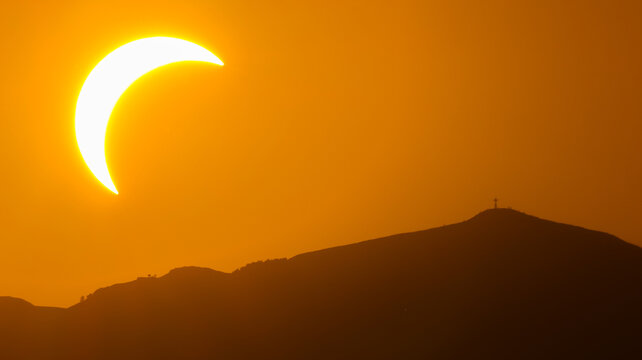 Geneva, Switzerland - 12 August 2026: View of a partial solar eclipse occurring over a mountain silhouette at sunset.