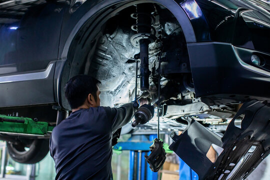 Selective focus to professional mechanic checking suspension, shock absorber, and drive shaft of a vehicle on a hydraulic lift in a garage repair service workshop.