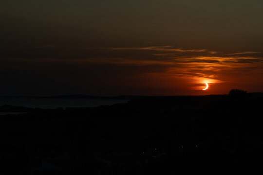 Son Bou, Spain - 12 August 2026: View of a partial solar eclipse at sunset over the horizon, with the sun partially obscured by the moon in the dark sky.