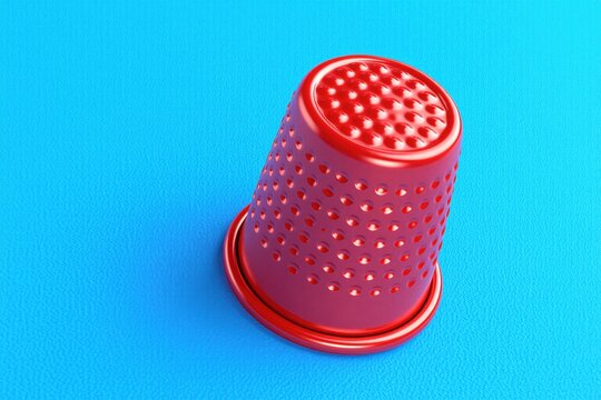 Shiny red sewing thimble sits on flat blue background. Metal protection tool for finger during needlework process. Tailor equipment for dressmaking embroidery, fabric repair. Creative craft item used