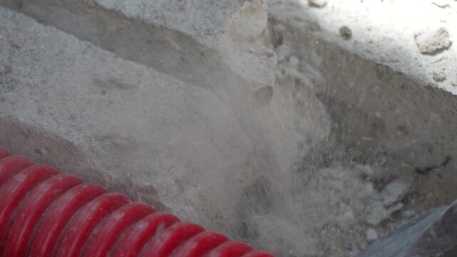 Renovation hammer chipping away solid concrete floor next to protective corrugated cable tubing. Macro close-up shot.
