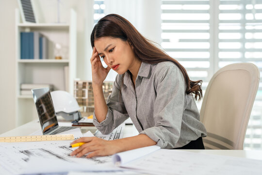 Stressful Professional construction engineer checking details on blueprint in construction site office.