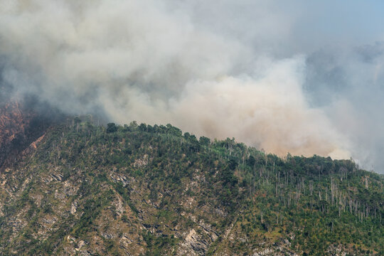 Smoke-covered forested slopes of Mount Amariana in Carnia, Friuli Venezia Giulia, Italy, during a wildfire emergency, showing firefighters&rsquo; rescue efforts and extensive damage.