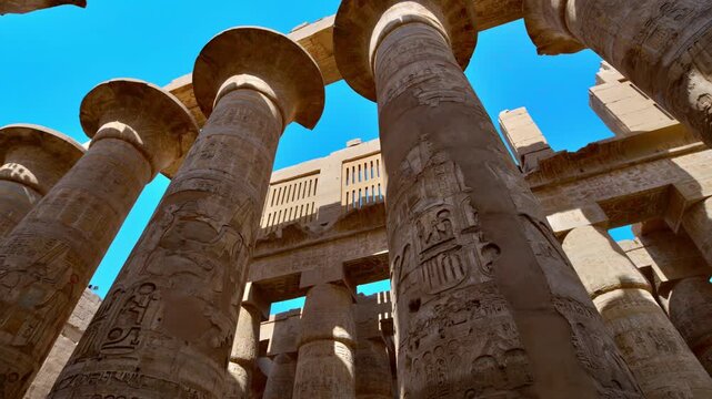 Karnak Temple in Luxor, Egypt. Massive hieroglyphic columns in Great Hypostyle Hall, Karnak Temple Luxor Egypt. Upward view of ancient carved pillars against blue sky.