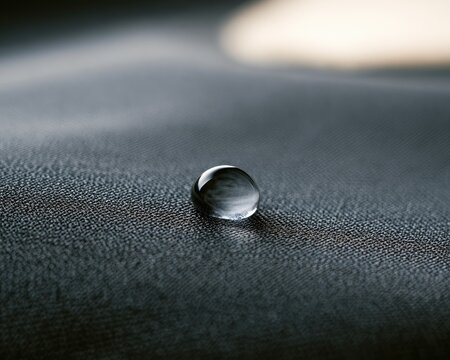Single water droplet rests on textured fabric, reflecting light