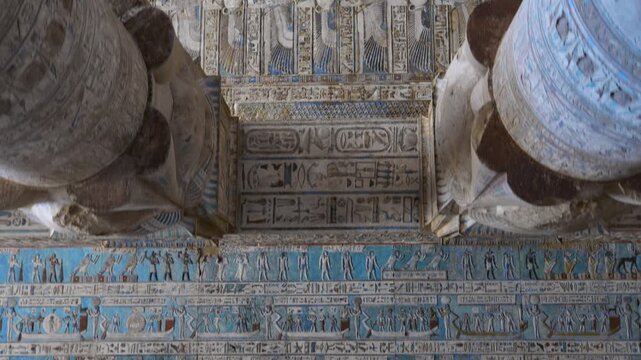 Dendera temple or Temple of Hathor. Painted columns with goddess faces and hieroglyphic ceiling of the hypostyle hall, ancient sandstone architecture with detailed carvings and blue painted astronomic