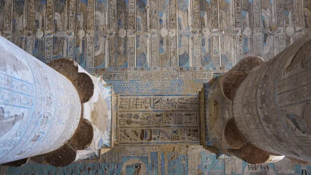 Dendera temple or Temple of Hathor. Painted columns with goddess faces and hieroglyphic ceiling of the hypostyle hall, ancient sandstone architecture with detailed carvings and blue painted astronomic
