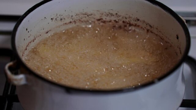 Deep frying french fries in a white pot on the gas stove.