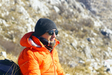 Fototapeta premium Close portrait of male hiker in orange jacket with softly blurred limestone slope behind. Depicts active longevity mindset, solo microadventure movement, and emotional wellbeing through nature connect