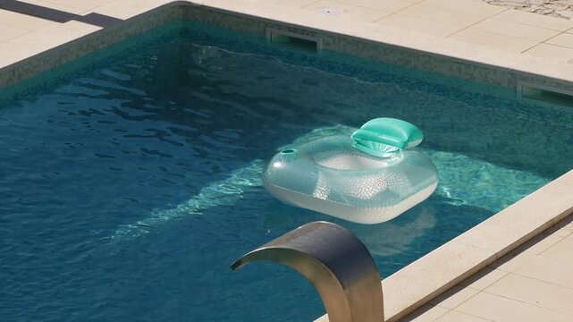 Inflatable pool floats in private villa pool during the summer. Sunlight reflects off surface of the water. Light plays on blue tiled bottom underwater. Gentle breeze. Pula, Croatia - August 15, 2026