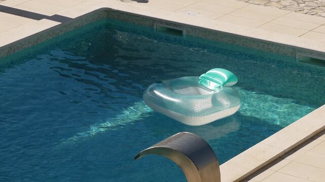 Inflatable pool floats in private villa pool during the summer. Sunlight reflects off surface of the water. Light plays on blue tiled bottom underwater. Gentle breeze. Slow motion