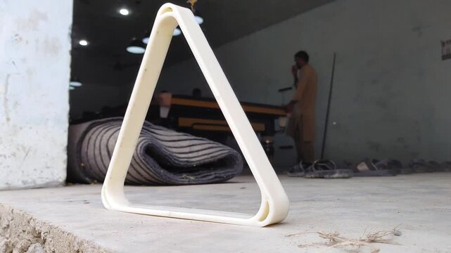 Billiard ball triangle rack on concrete floor. White plastic pool rack standing upright. Billiard club interior context.