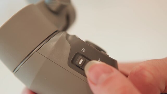 Close-up of thumb pressing textured rocker switch on handheld gray device, moving control toward plus icon to raise setting, with fingertip pressure, slight depression, and clear detail