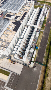 Aerial view of a modern data center featuring industrial cooling units, rooftop solar panels, and a secure fenced perimeter in Melegnano, Lombardy, Italy.