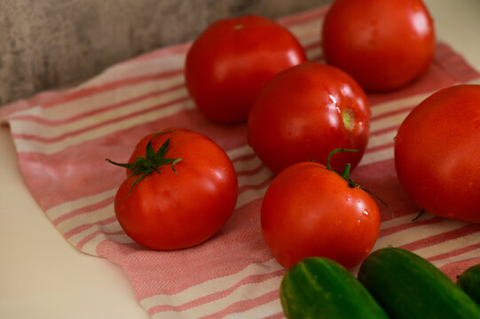 Freshly picked tomatoes rest on a striped cloth alongside vibrant cucumbers
