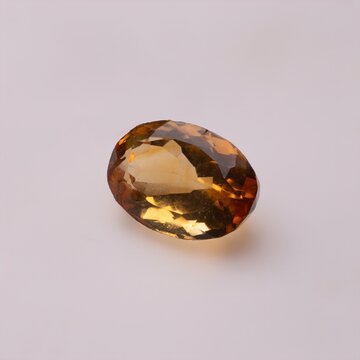 Oval cut yellow citrine gemstone with faceted surfaces on a plain white background.