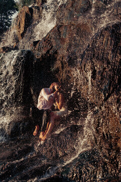Passionate couple kissing behind waterfall spray in warm sunset light